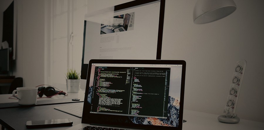 Laptop displaying code beside a monitor showing a website preview, representing Parsian Holdings' web and mobile development work